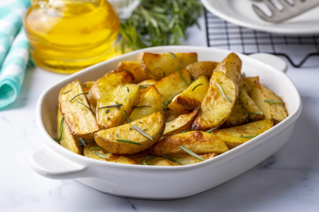 Patate al forno in una pirofila bianca condite con rosmarino.